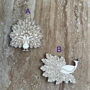 May include: Two wooden peacock cutouts. One peacock is facing forward with its tail feathers fully displayed. The other peacock is in profile, with its tail feathers fanned out. Both are made of light-colored wood.