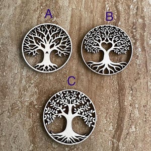 May include: Three white wooden tree of life cutouts in a circular design. Each cutout features a different tree design, with variations in the branches and leaves. The cutouts are labeled A, B, and C.