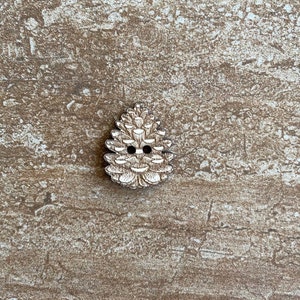 May include: A white wooden button shaped like a pine cone with two holes for sewing.