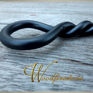May include: Black metal fireplace poker with a twisted handle and a loop at the end. The poker is resting on a wooden surface.