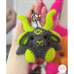 May include: A crocheted keychain featuring a gray and neon green goat-like creature with a pentagram on its head. The keychain has a silver ring and a tag. The text on the image says "PLEASE NOTE THIS IS NOT A PHYSICAL PRODUCT THE DIGITAL CROCHET PATTERN".