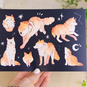 May include: A dark blue print featuring illustrations of orange-coloured wolves in various poses, with white stars and a crescent moon. The artwork has a whimsical, illustrative style.