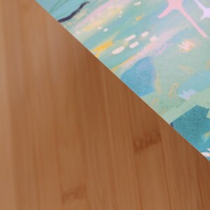 May include: A section of a colorful abstract art print with a light brown wooden surface in the background. The print features a mix of teal, blue, pink, and yellow brushstrokes, with star-like shapes.