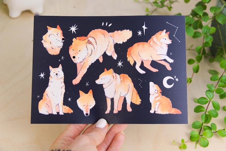 May include: A dark blue print featuring illustrations of orange-coloured wolves in various poses, with white stars and a crescent moon. The artwork has a whimsical, illustrative style.