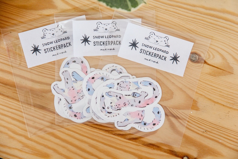 Puede incluir: Una bolsa de pl&aacute;stico transparente llena de pegatinas de leopardo de las nieves de colores. Las pegatinas est&aacute;n dibujadas a mano y presentan una variedad de poses. La bolsa tiene una etiqueta que dice "Snow Leopard Stickerpack made in world."