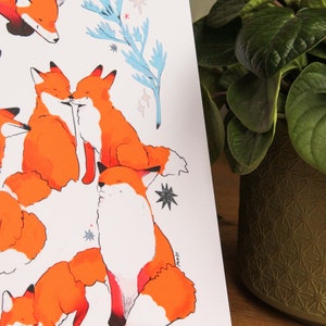 May include: A white background with a repeating pattern of orange foxes. The foxes are in various poses, including cuddling, sleeping, and sitting up. The background also features blue and white floral elements.