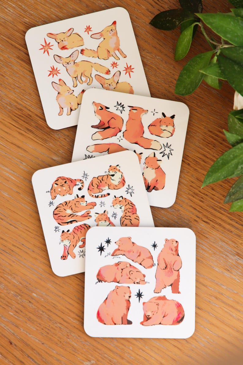 May include: Set of four square coasters with animal illustrations. Each coaster features a different animal: foxes, tigers, bears, and rabbits. The animals are in shades of orange and brown, with star accents on a white background.