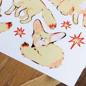 May include: A set of four illustrated fennec foxes with orange and yellow fur. The foxes are in various poses, including sitting, standing, and looking up. The background is white with red starbursts.