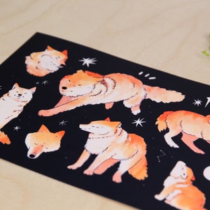 May include: A black rectangular print with watercolour illustrations of orange and white wolves in different poses. The design includes stars and a crescent moon, creating a celestial theme. The artwork has a whimsical, artistic style.