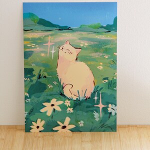 May include: A whimsical art print featuring a cream-colored cat basking in a field of flowers under a starry night sky. The illustration has a soft, dreamy aesthetic with pastel colors and sparkling accents. The artist's signature, MADI, is visible.