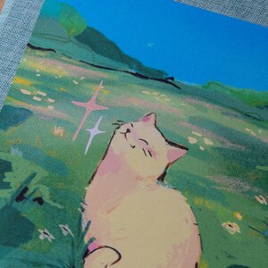 Puede incluir: Una impresi&oacute;n que muestra un gato sonriente en un campo de flores. El gato es de color amarillo claro con acentos rosados, disfrutando del sol. El fondo incluye colinas verdes y un cielo azul brillante, creando una escena serena.