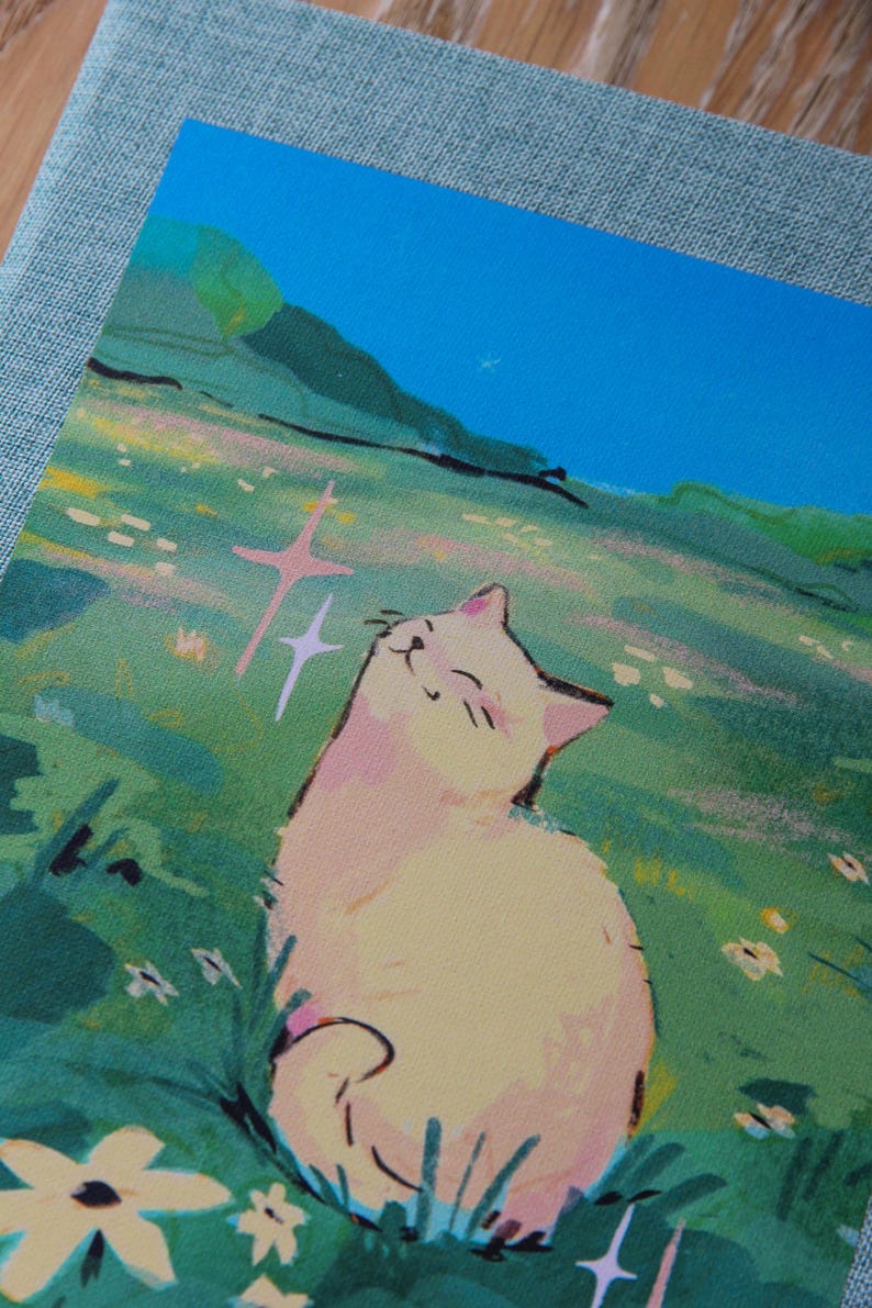 Puede incluir: Una impresi&oacute;n que muestra un gato sonriente en un campo de flores. El gato es de color amarillo claro con acentos rosados, disfrutando del sol. El fondo incluye colinas verdes y un cielo azul brillante, creando una escena serena.
