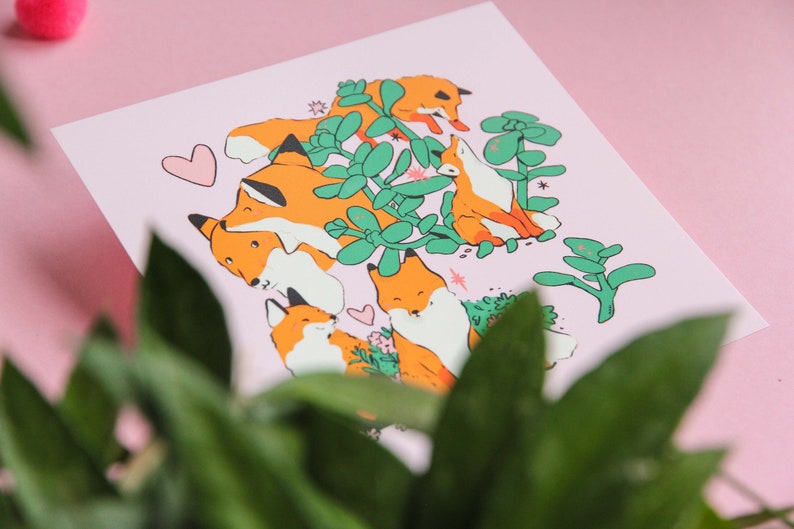 May include: A pink background with a print of five orange foxes surrounded by green plants. The foxes are in various poses, some are looking at the viewer, some are looking away. There are small pink hearts scattered around the foxes.