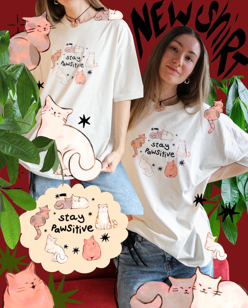 Puede incluir: Camiseta de color crema con una ilustraci&oacute;n de gato y las palabras "stay Pawsitive". La camiseta presenta varios dise&ntilde;os de gatos de dibujos animados en tonos de rosa, marr&oacute;n y blanco. El fondo es rojo oscuro con follaje verde.