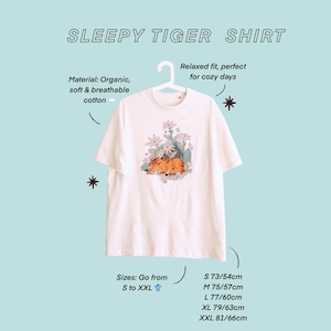 May include: Cream-colored t-shirt with a graphic of a sleeping tiger surrounded by flowers. The shirt is made of organic, soft, and breathable cotton. The text "SLEEPY TIGER SHIRT" is at the top. Sizes range from S to XXL, with measurements in centimeters.