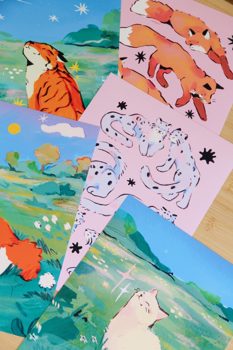 May include: A collection of art prints featuring illustrations of animals. The prints showcase a tiger, foxes, snow leopards, and a cat, with a color palette of orange, pink, blue, and green. The artwork has a whimsical, illustrative style.