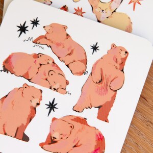 May include: Two white square cards with illustrations of animals. One card features foxes and stars in orange and yellow. The other card has pink bears and black stars. The cards are on a wooden surface.