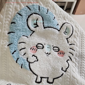 Könnte beinhalten: Weißer Strickstoff mit einem blauen und weißen gestickten Comic-Kaninchen mit dem Text "可愛い" in Japanisch.