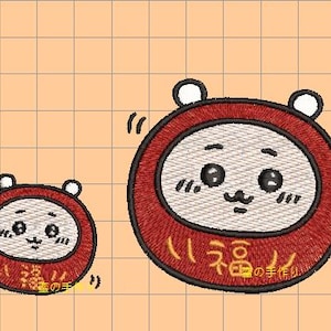Könnte beinhalten: Zwei gestickte Daruma-Puppen, eine große und eine kleine, mit roten Außenkreisen und weißen Gesichtern. Die Puppen haben schwarze Augen, einen kleinen Schnurrbart und japanische Schriftzeichen für "Glück" und "handgemacht".