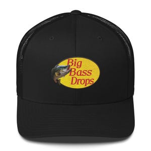 Op de afbeelding: Zwarte truckerpet met een mesh achterkant en een gebogen klep. De voorkant heeft een geel ovaal logo met de rode tekst "Big Bass Drops" en een visafbeelding.