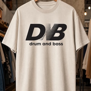 May include: A beige short-sleeve t-shirt featuring a black graphic on the chest. The graphic displays the letters D and B with horizontal motion lines between them, followed by the text drum and bass in a simple sans-serif font below.