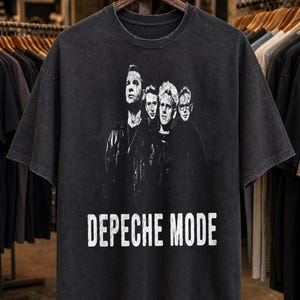 May include: A charcoal grey short-sleeve t-shirt featuring a distressed white graphic print of the band Depeche Mode. The design includes a black and white photograph of the four band members above the text DEPECHE MODE in a bold, sans-serif font.
