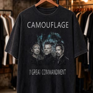 Peut inclure: Un t-shirt noir à manches courtes avec une impression graphique représentant trois hommes. Le texte CAMOUFLAGE est imprimé en blanc au-dessus des hommes, et le texte THE GREAT COMMANDMENT est imprimé en blanc en dessous sur fond bleu.