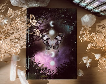 May include: A purple and black butterfly with white accents is centered on a card with a dark background. The butterfly is surrounded by three moons in various phases. The card is on a wooden surface with white flowers and crystals.