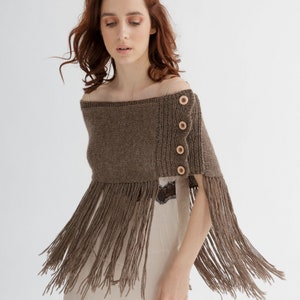 May include: A brown knitted shawl with fringe and wooden buttons. The shawl is draped over a person's shoulders.