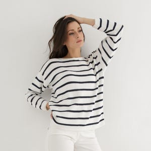 Può includere: Un maglione a righe bianche e blu navy con scollo a barca.