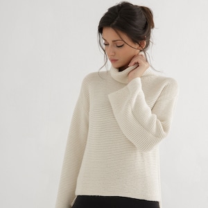 May include: A white turtleneck sweater with a ribbed texture and wide bell sleeves.