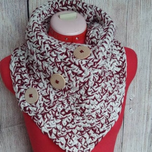 May include: A crocheted cowl in burgundy and white with three wooden buttons. The cowl is displayed on a red mannequin.