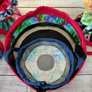 May include: A set of nested fabric storage bins with a tie-top closure. The bins are made of different tie-dye patterns in shades of blue, green, and pink. The bins are lined with a gray fabric and have a black ribbon tie.