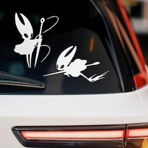 Op de afbeelding: Witte vinyl auto sticker met twee gestileerde figuren. Eén figuur staat met een zwaard, de andere in een dynamische pose. De figuren hebben een kenmerkend insectachtig uiterlijk, ideaal voor videogame liefhebbers.
