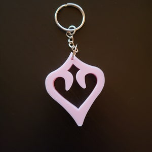 Peut inclure: Un porte-clés en plastique rose avec un design en forme de cœur. Le cœur a une découpe au centre, créant une forme de cœur plus petite à l'intérieur du plus grand.