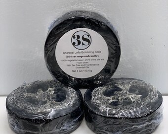 Puede incluir: Tres barras de jabón exfoliante de luffa de carbón vegetal negras envueltas en plástico. Las barras de jabón están etiquetadas con "3S Charcoal Luffa Exfoliating Soap 3 sisters soaps and candles 100% vegetable based, 20% of the oils are From olives With Tea Tree and Frankincense Essential Oils Net 4 oz/113.4 g"