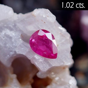 May include: A vibrant pink pear-shaped gemstone, weighing 1.02 carats, displayed on a white rock.