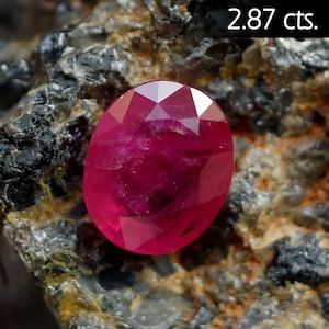 Może przedstawiać: Czerwony rubin, o wadze 2,87 karatów, umieszczony na szorstkiej, ciemnoszarej skale.