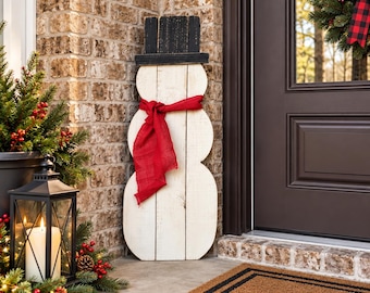 May include: A decorative wooden snowman figure constructed from vertical white planks, featuring a black top hat and a bright red fabric scarf tied around its neck. The snowman stands upright with a rounded three-tiered body design.