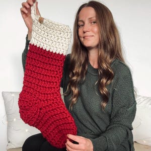 Peut inclure: Une chaussette de Noël crochetée à la main avec un corps rouge vif et un revers de couleur crème contrastant sur le dessus. La chaussette comprend une petite étiquette rectangulaire marron clair fixée au bord supérieur pour la suspendre.