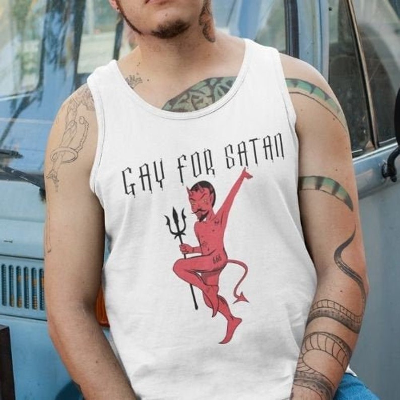 May include: White tank top with the text "GAY FOR SATAN" in black, featuring a red devil graphic with a trident. The devil graphic has the number "666" on its leg. The tank top is a casual garment.