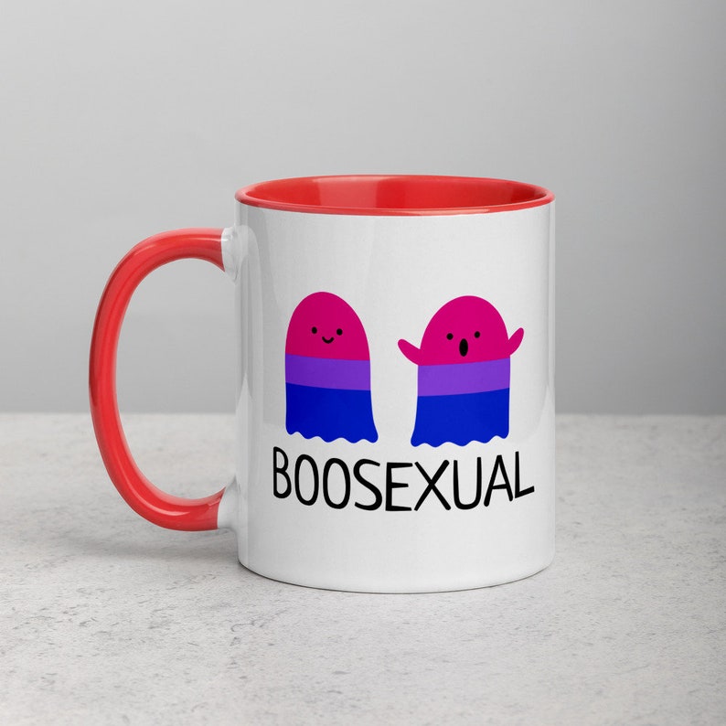 May include: White ceramic mug with a red rim and handle. The mug features two cartoon ghosts with the bisexual pride flag colors. The text "BOOSEXUAL" is printed below the ghosts.