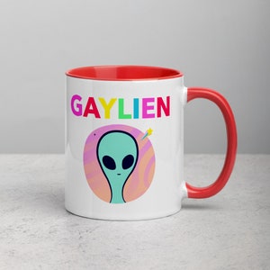 May include: White ceramic mug with a red rim and handle. The mug features a graphic of a green alien with a rainbow coloured word "GAYLIEN" above it.
