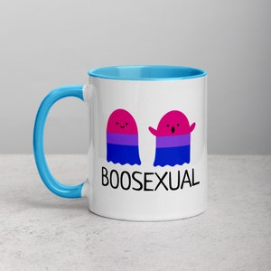May include: White ceramic mug with a blue rim and handle. The mug features two cartoon ghosts with the bisexual pride flag colors. The text "BOOSEXUAL" is printed below the ghosts.