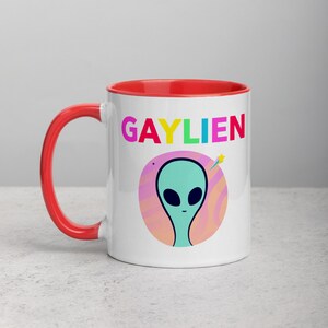 May include: White ceramic mug with a red rim. The mug features a graphic of a green alien with a rainbow coloured word "GAYLIEN" above it.