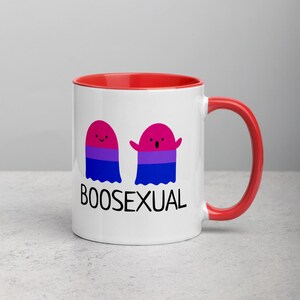 May include: White ceramic mug with a red rim and handle. The mug features two cartoon ghosts with the bisexual pride flag colors. The text "BOOSEXUAL" is printed below the ghosts.
