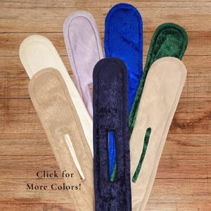 May include: A collection of six long, narrow, plush fabric hair styling tools in various colors including cream, lavender, royal blue, dark navy, forest green, and beige, each featuring a central vertical slit for hair insertion.