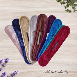 May include: A collection of colorful hair bun makers in various shades, including pink, navy, tan, gray, burgundy, purple, blue, teal, and red. Each hair accessory has a rectangular shape with a central slit. The text "Sold Individually" is at the bottom.
