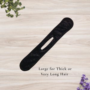 May include: A black hair styling tool with a long, slender shape and a central opening. The text "Large for Thick or Very Long Hair" is printed below the tool. The tool is designed for use with thick or long hair.
