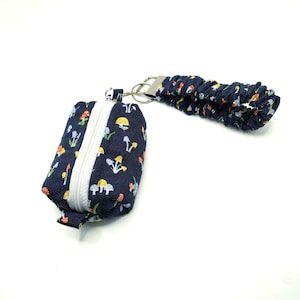 May include: A small, navy blue pouch with a white zipper and a matching wrist strap. The pouch and strap are decorated with a colorful mushroom pattern. The pouch is attached to a silver-colored metal ring.